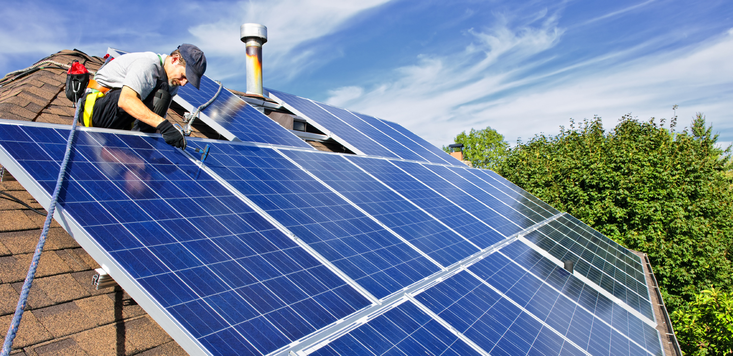 [Man installing alternative energy photovoltaic solar panels on roof