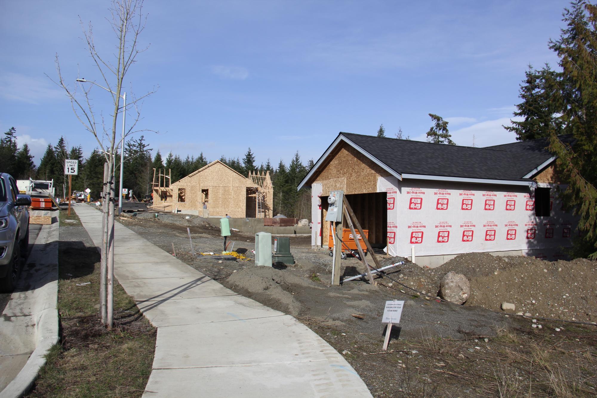 [Two houses under construction with completed sidewalk in front]